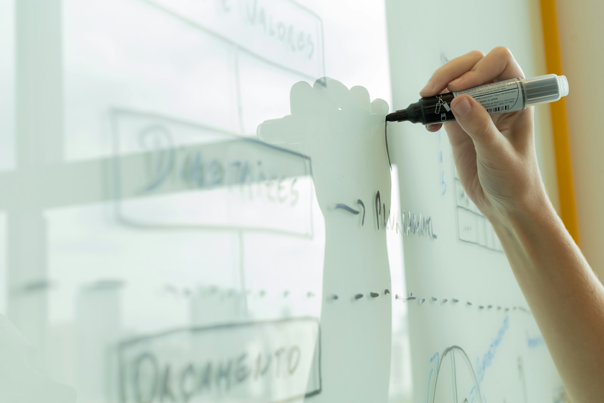 Mano dibujando un diagrama con un marcador sobre un tablero de vidrio.